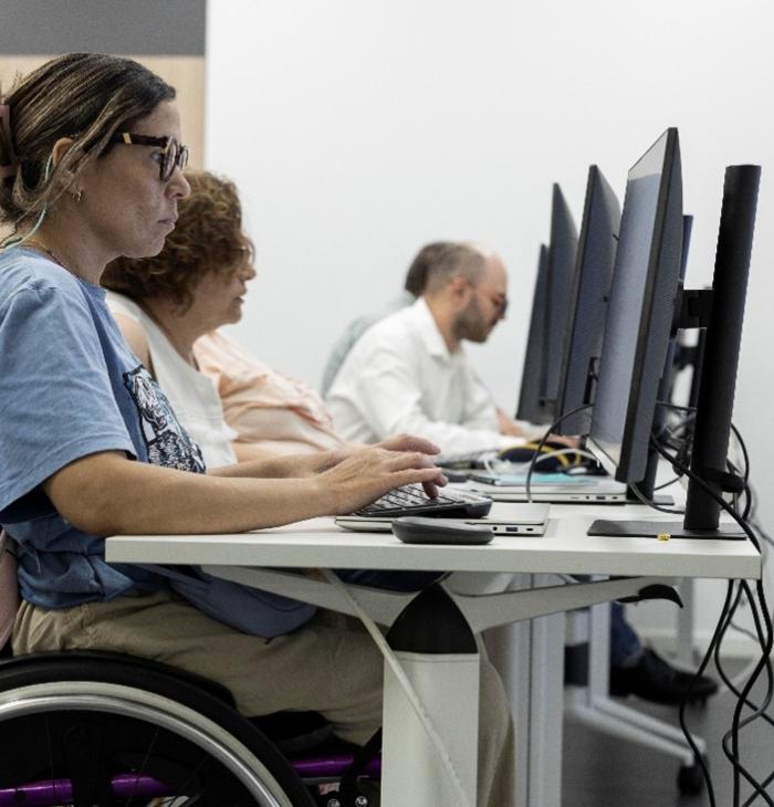 Una mujer en silla de ruedas en el aula de formación de Por Talento Digital formándose en NNTT